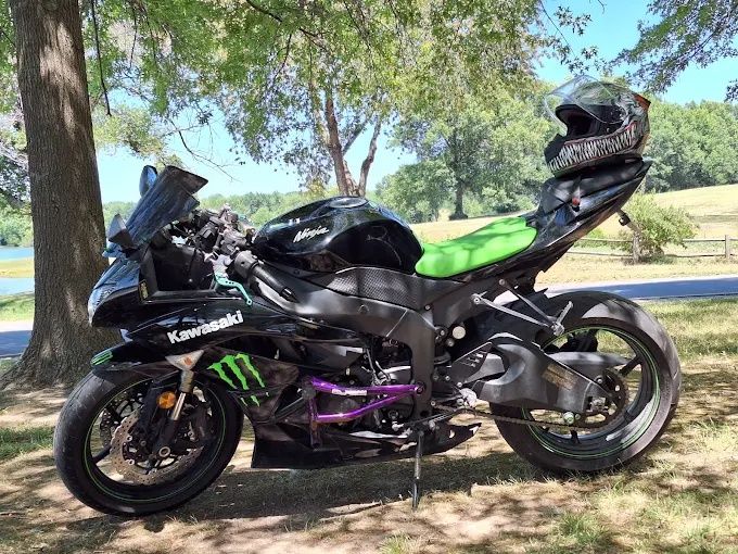 Black sport motorcycle with neon green seat parked under trees on grass by a roadside.