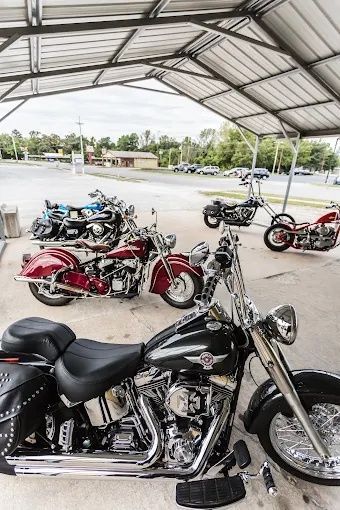 Motorcycles parked under a metal canopy in an open lot, including a black cruiser in the foreground.