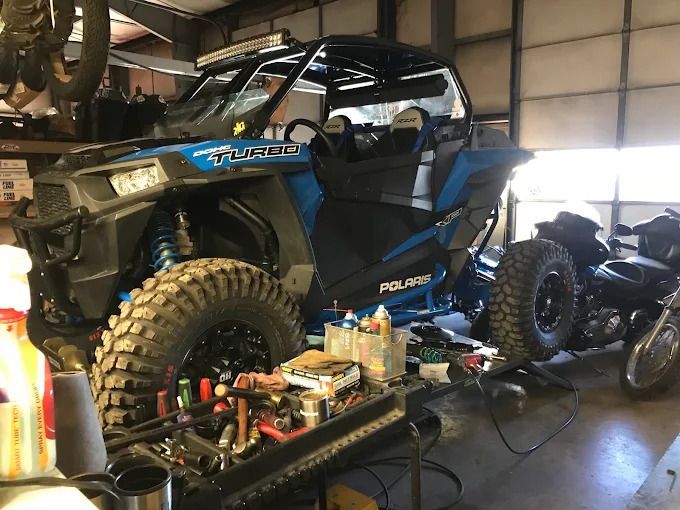 Blue Polaris off-road vehicle in a garage, with tools and motorcycle nearby.