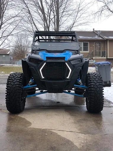 Blue and black off-road ATV parked on a wet driveway in front of a house