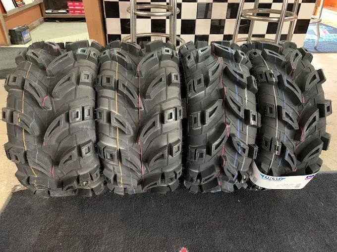 Stack of black knobby off-road tires stored indoors on a floor.