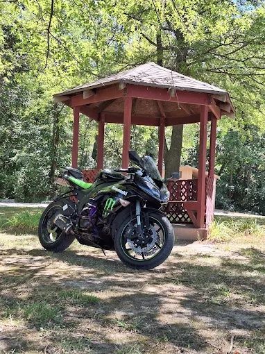 Black and green sport motorcycle parked in front of a red wooden gazebo in a wooded area.