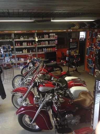 Motorcycles displayed inside a garage-like shop with shelves of parts and supplies