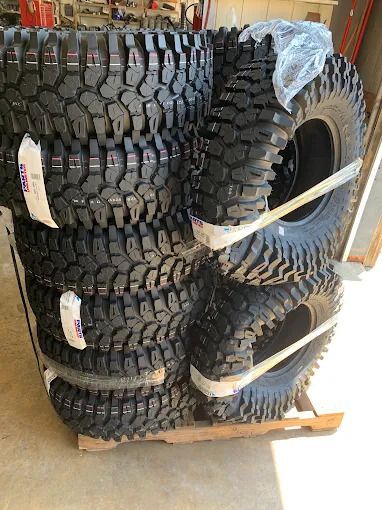Stacked black off-road tires on a wooden pallet in a warehouse.