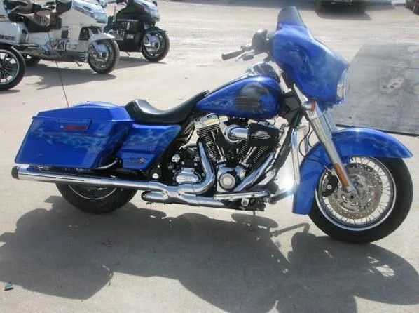 Blue motorcycle parked on pavement, side view, with chrome details and windshield