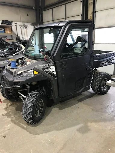 Black off-road utility vehicle in a workshop, with large tires and a rear cargo bed.