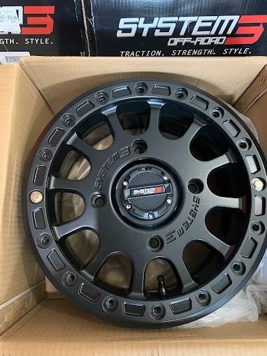 Black off-road alloy wheel rim in a cardboard box with SYSTEM 5 labels behind it