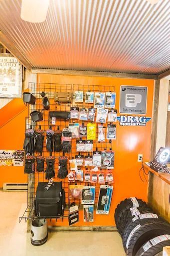 Orange retail display wall with hanging accessories, packaged items, and a black bag under a corrugated metal ceiling