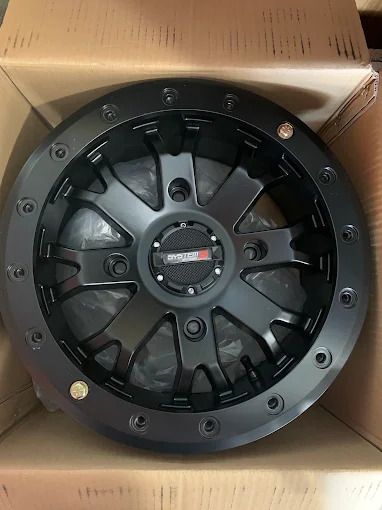 Black multi-spoke car wheel rim in a cardboard box, viewed from above.