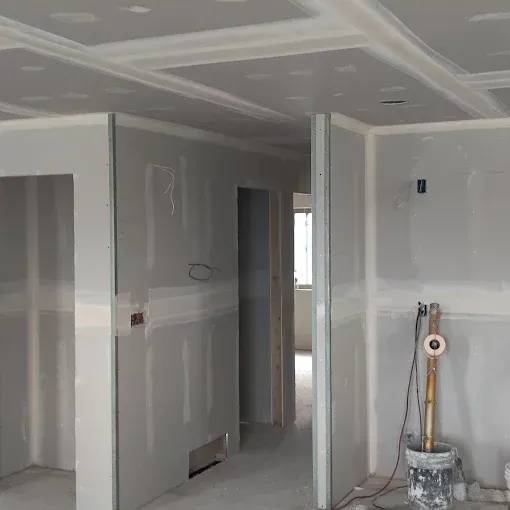 Interior view of a building under construction, showing drywall walls and ceiling, with unfinished areas.