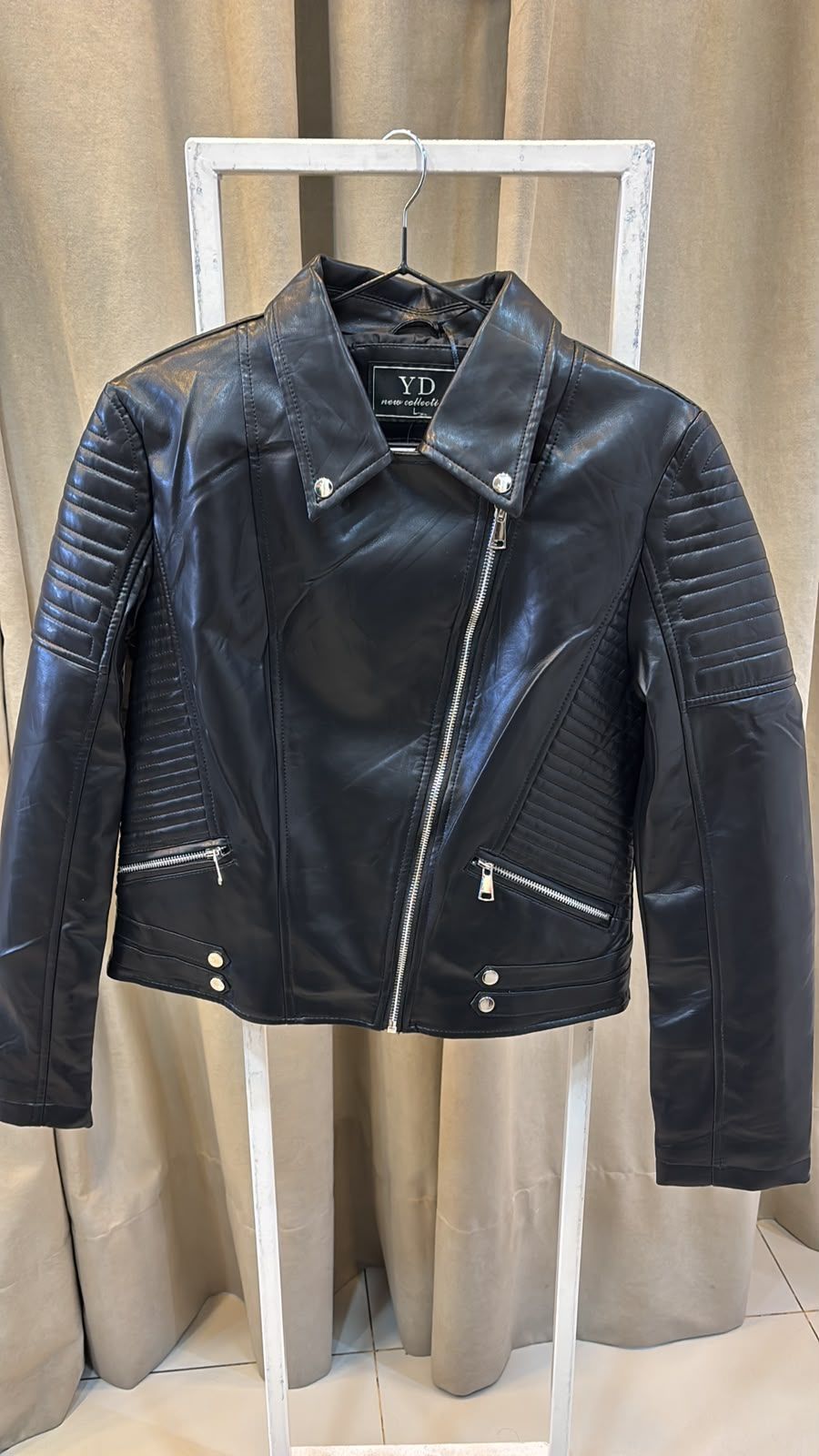 Chaqueta de motorista de cuero negro en una percha blanca frente a unas cortinas beige.