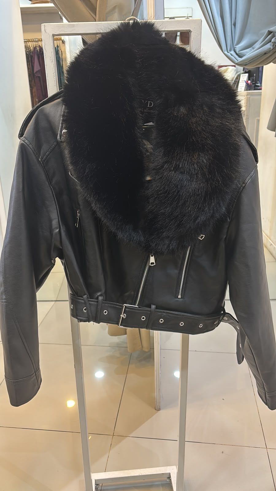 Chaqueta negra con capucha de piel sintética y cremalleras plateadas colgada en un perchero en una boutique.