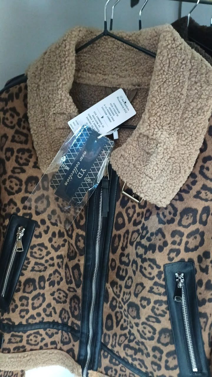Abrigo con estampado de leopardo y cuello de piel sintética color camel colgado en una percha negra, con etiquetas adjuntas.