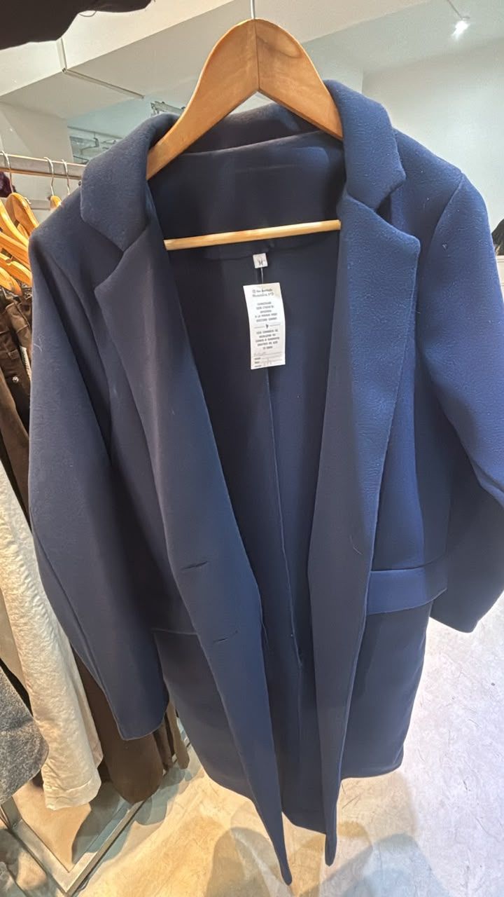 Un abrigo azul colgado en una percha de madera en una tienda de ropa.