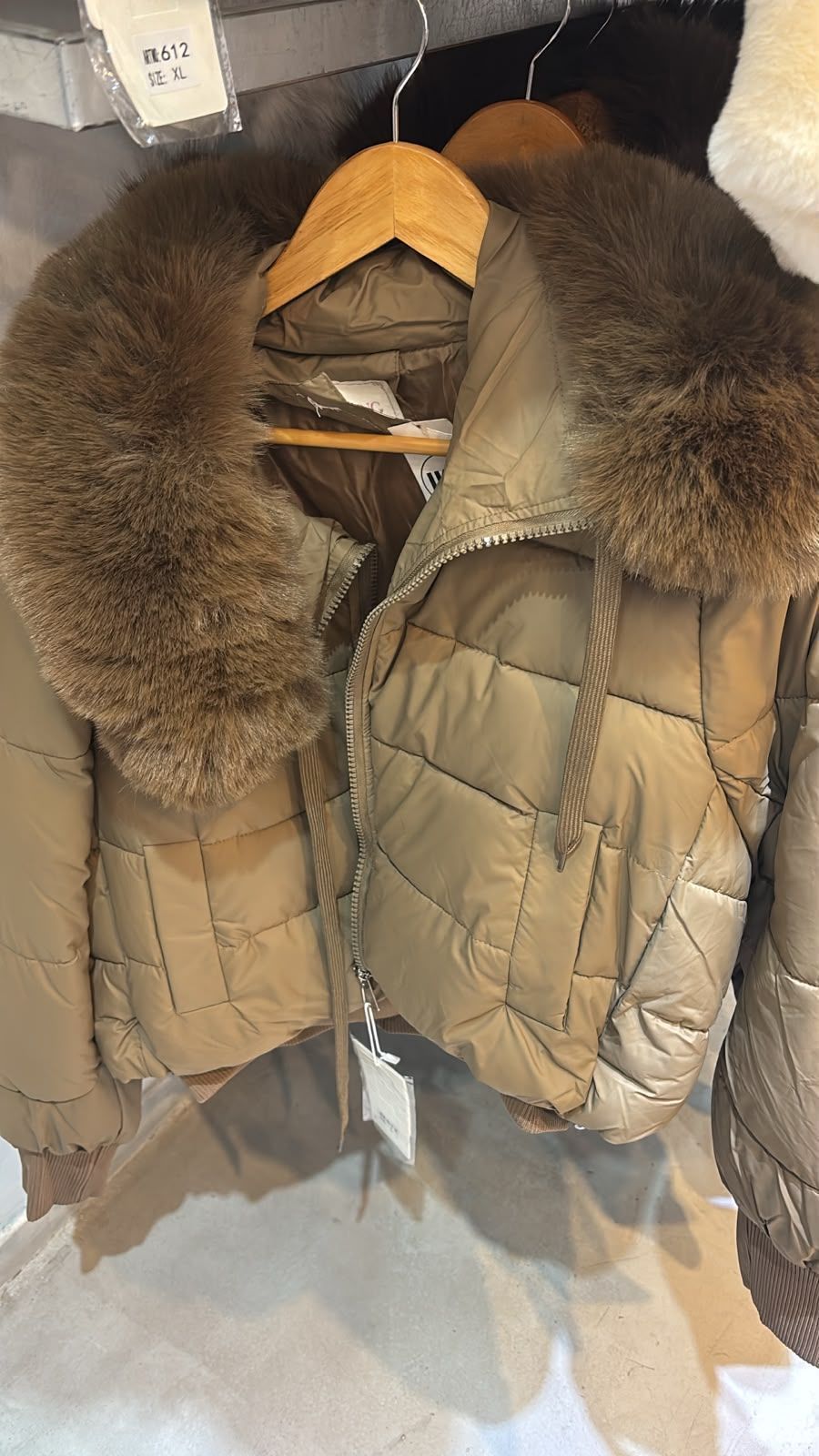Dos chaquetas acolchadas color canela con capuchas ribeteadas de piel colgadas en perchas de madera en un armario.