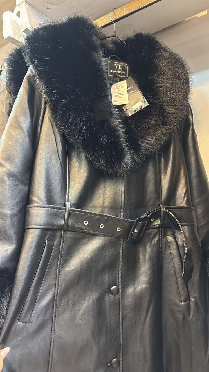 Abrigo de cuero negro con gran cuello y cinturón de piel negra, colgado en un perchero.