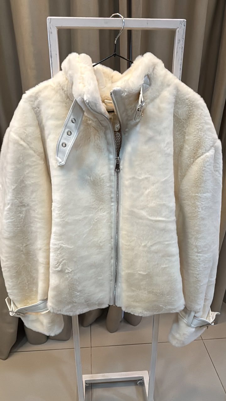 Chaqueta blanca de pelo sintético con cremallera colgada en un perchero en una tienda.