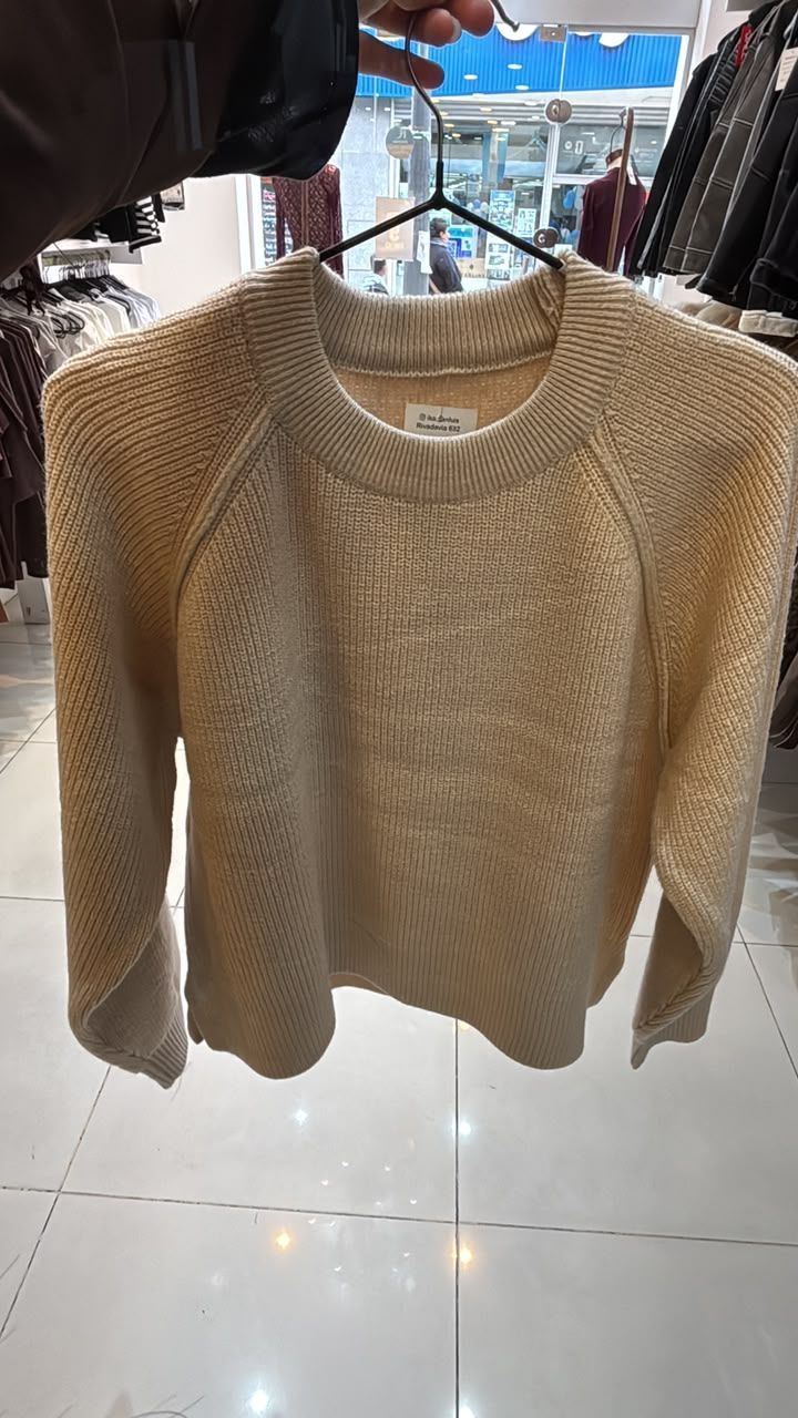 Un suéter de punto beige colgado en un perchero en una tienda de ropa.