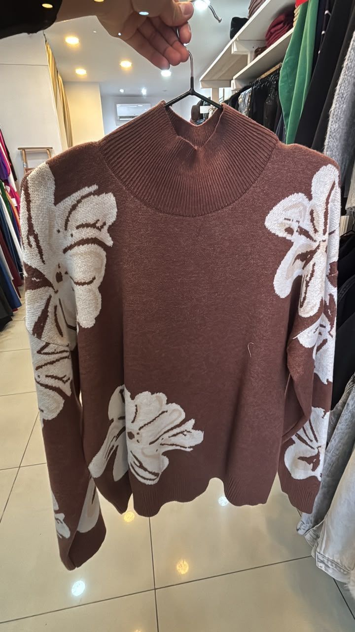 Suéter marrón con grandes estampados florales blancos en un perchero de una tienda.