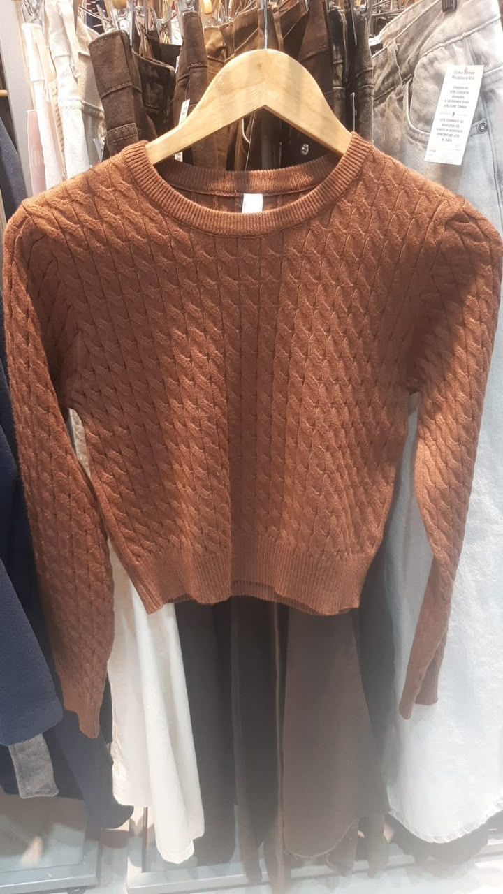 Suéter marrón de punto trenzado de manga larga en una percha de madera en una tienda de ropa.