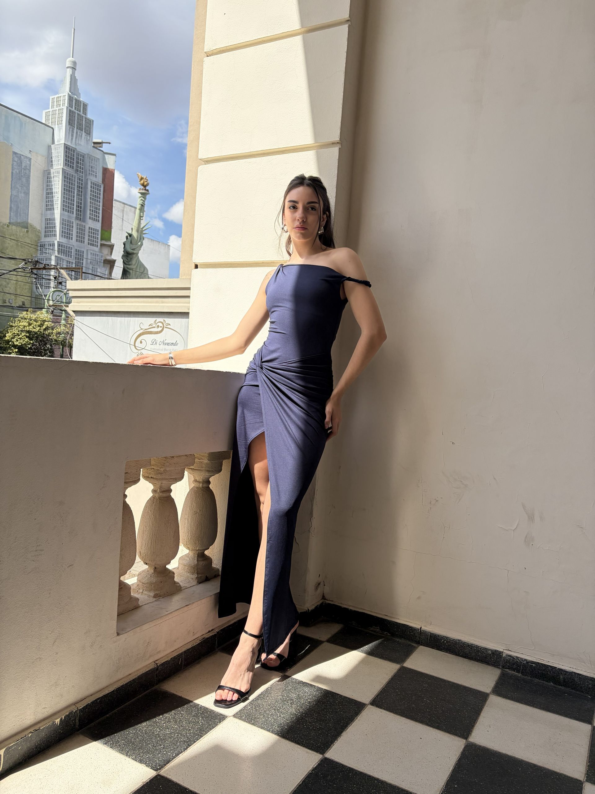 Persona posando con un vestido azul largo en un balcón de un edificio.