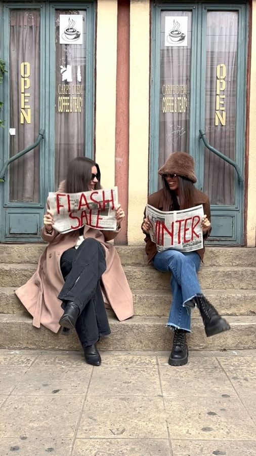 Dos personas están sentadas frente a una tienda sosteniendo carteles que dicen 