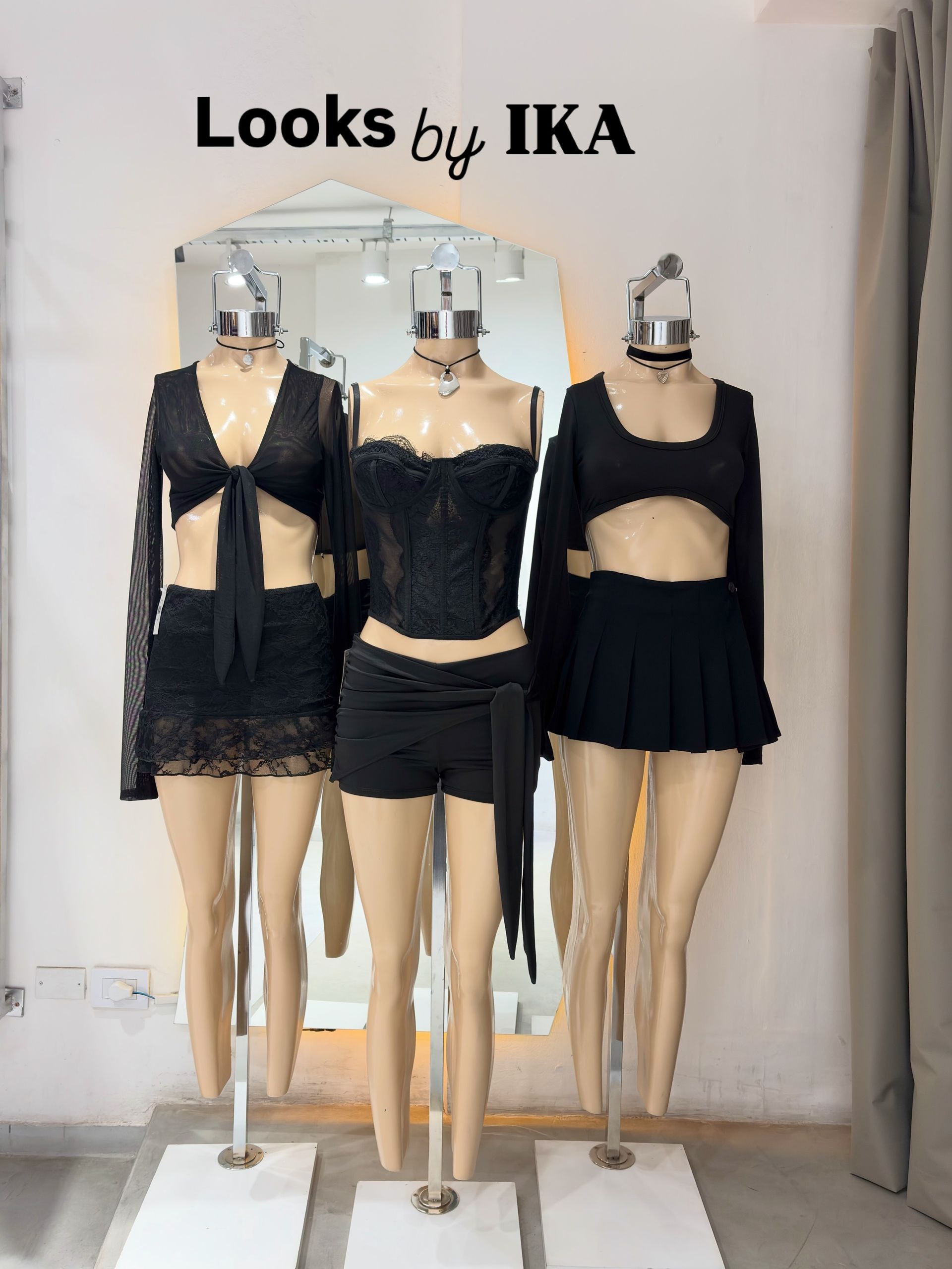 Tres maniquíes con conjuntos de encaje negro se exhiben en el escaparate de una boutique bajo el letrero “Looks by IKA”.