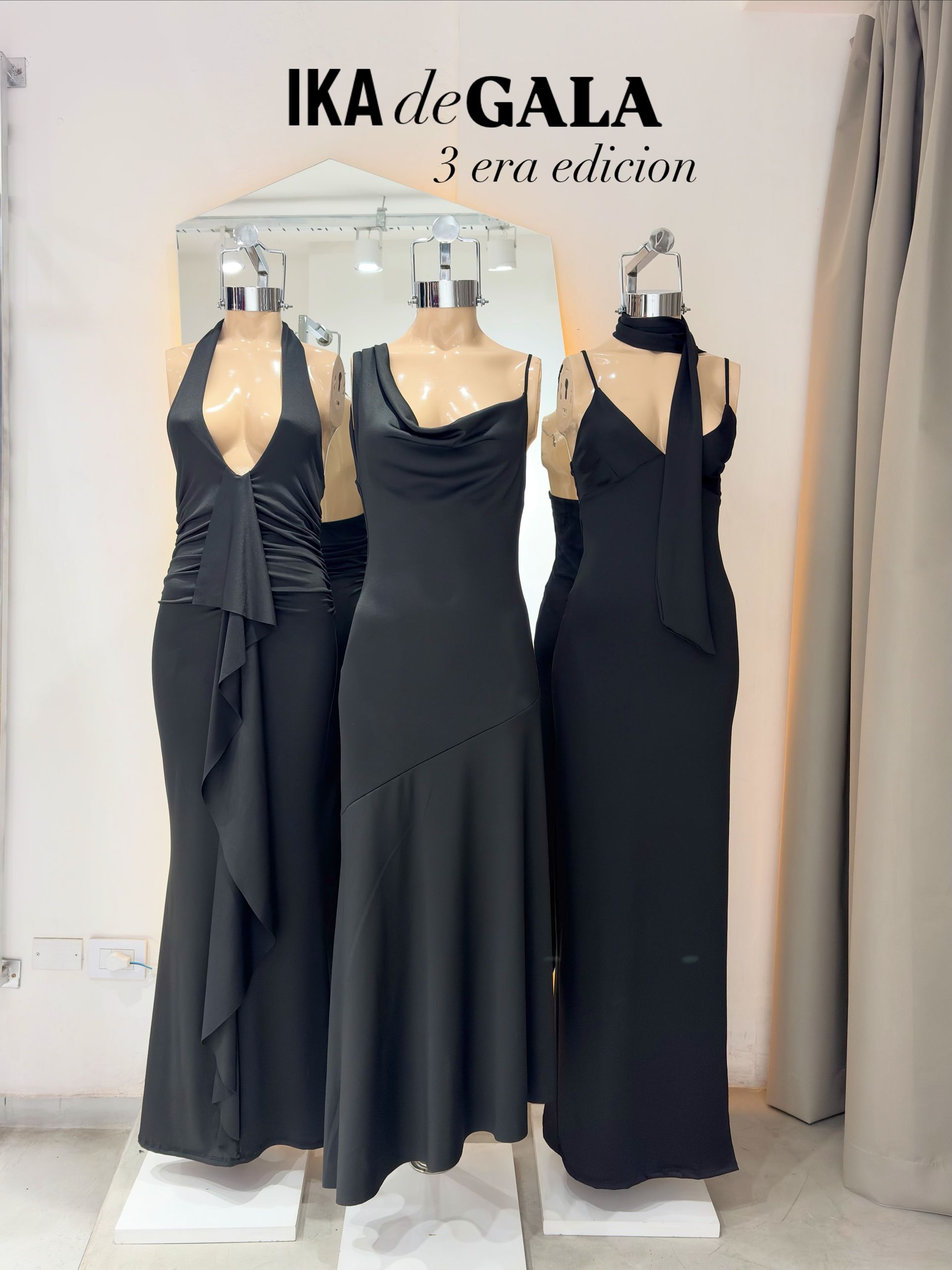 Tres vestidos de noche negros sobre maniquíes en el escaparate de una boutique, con el letrero de IKA de GALA encima.
