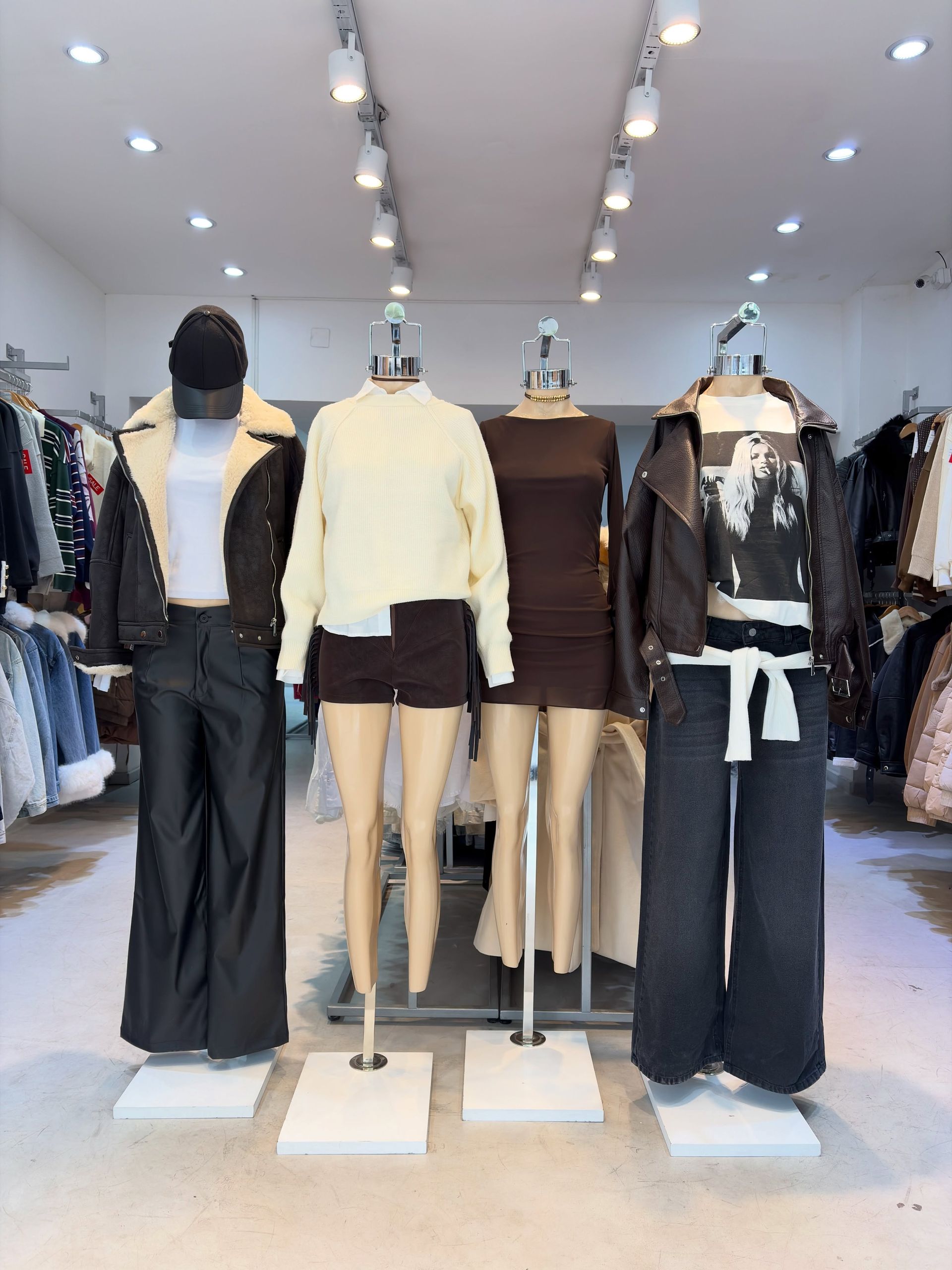 Escaparate de una tienda de ropa con tres maniquíes vestidos con conjuntos negros y beige bajo luces de techo.