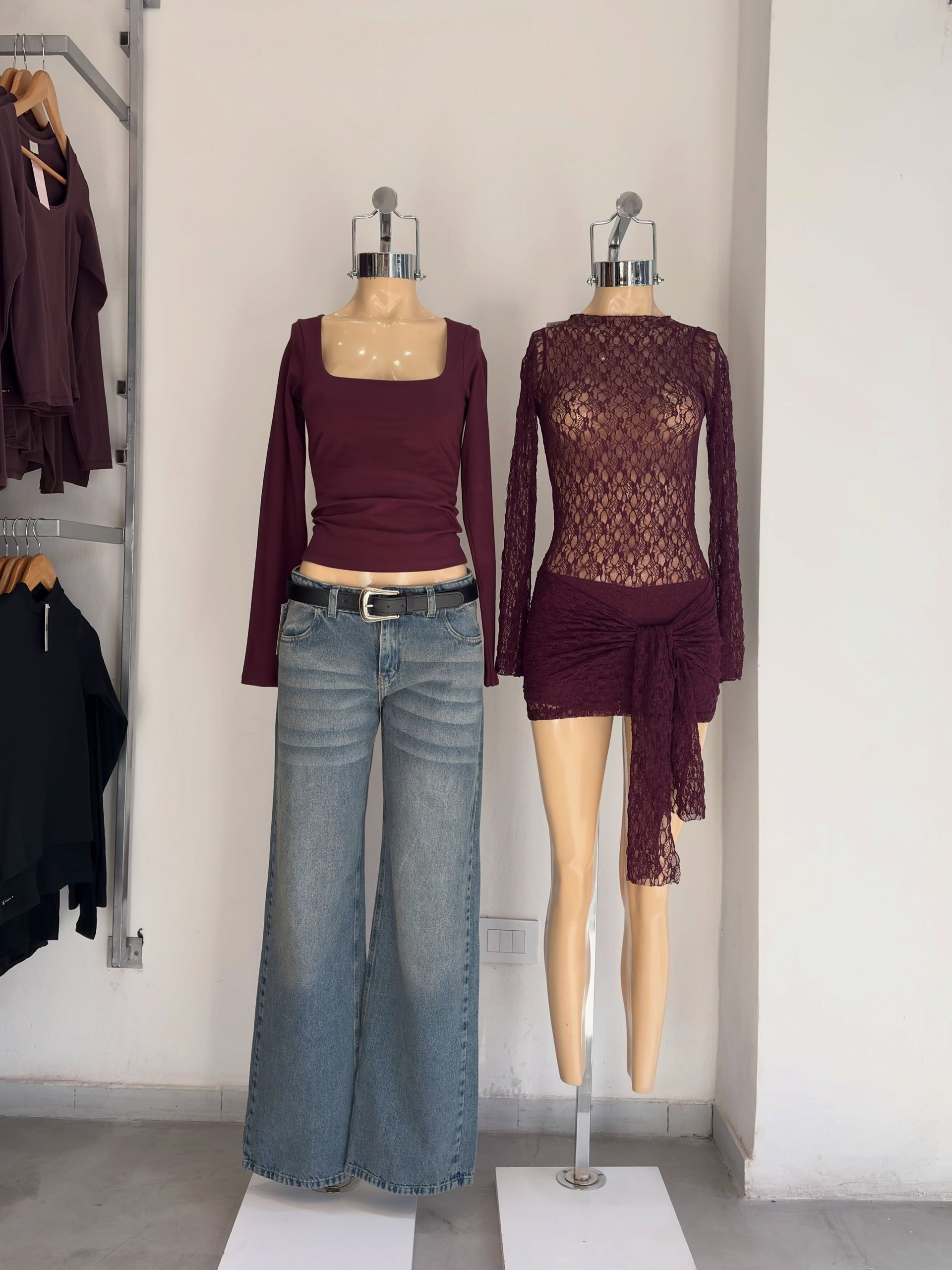 Dos maniquíes que exhiben blusas color burdeos y pantalones vaqueros azules en una tienda de ropa.