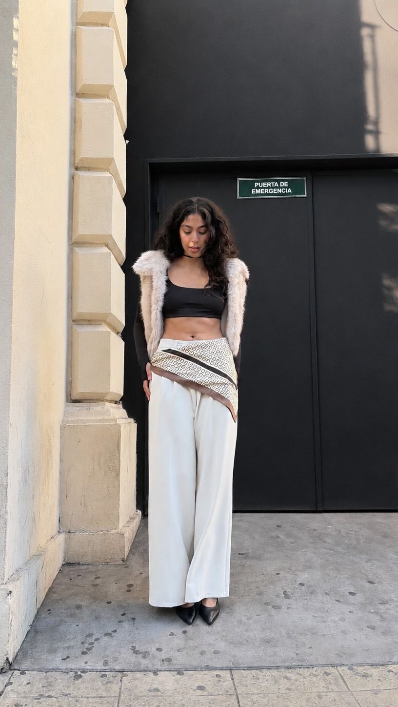 Mujer con blusa negra y pantalones blancos de pie junto a la entrada de un edificio.