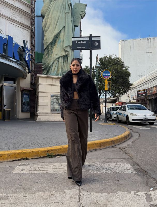 Una persona con un abrigo oscuro camina por un paso de peatones en la ciudad, cerca de una estatua