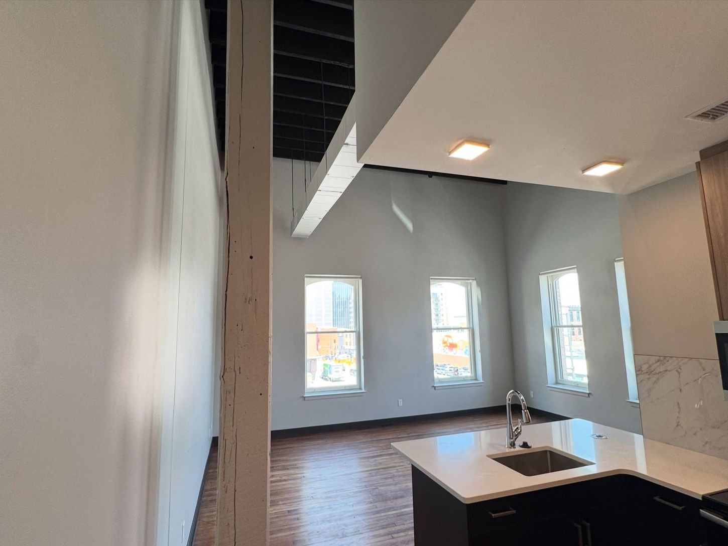 Modern open kitchen with white island, wood floors, gray walls, and large windows.