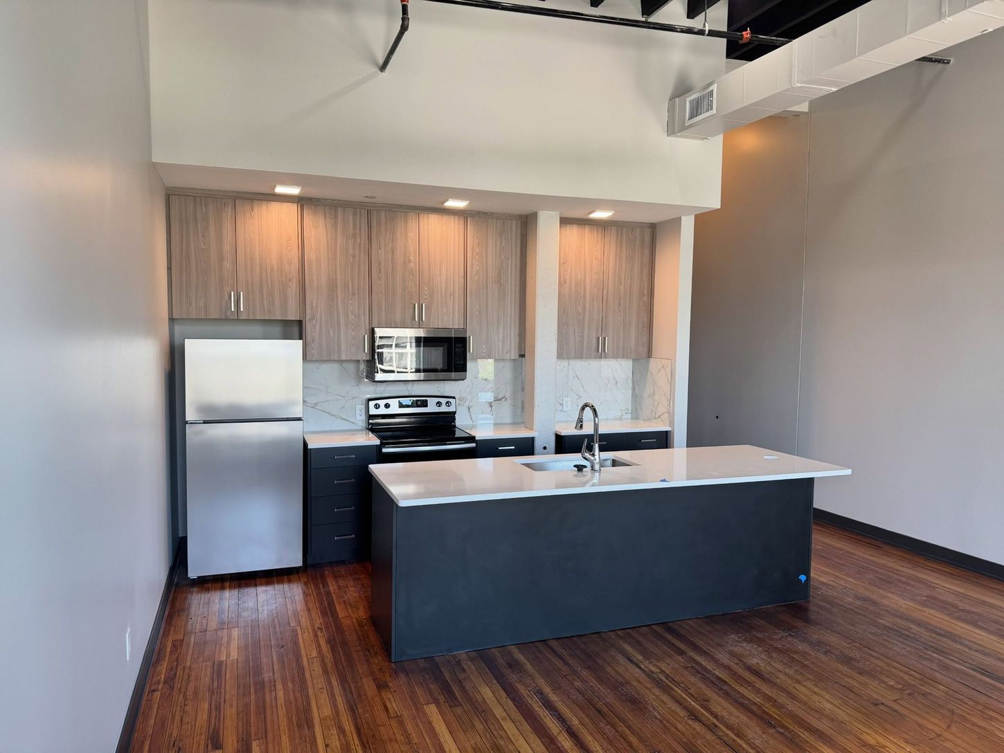 Modern kitchen with stainless appliances, dark island, wood floors, and white walls