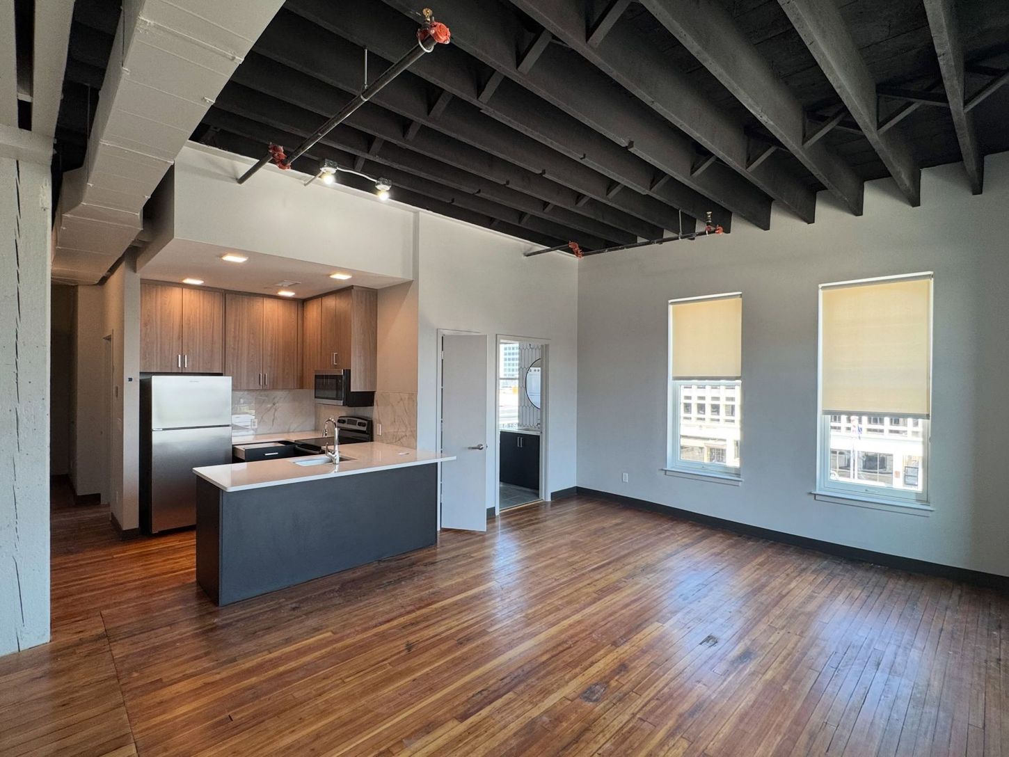 Open-concept loft apartment with hardwood floors, exposed ceiling beams, kitchen island, and large windows