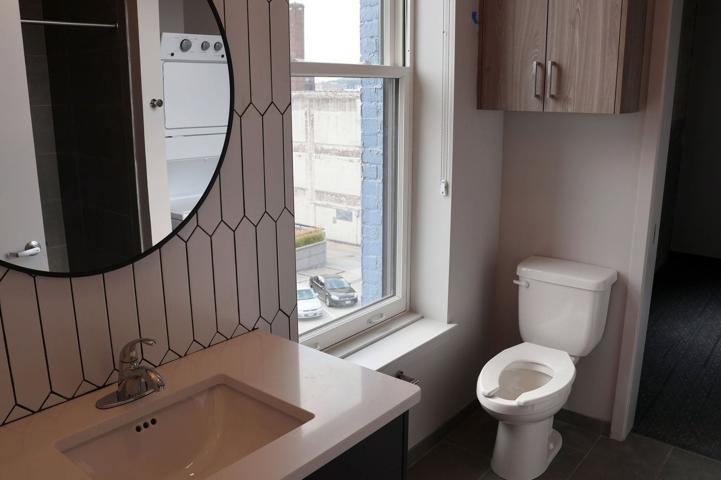 Small bathroom with sink, patterned wall mirror, window, toilet, and wood cabinets.