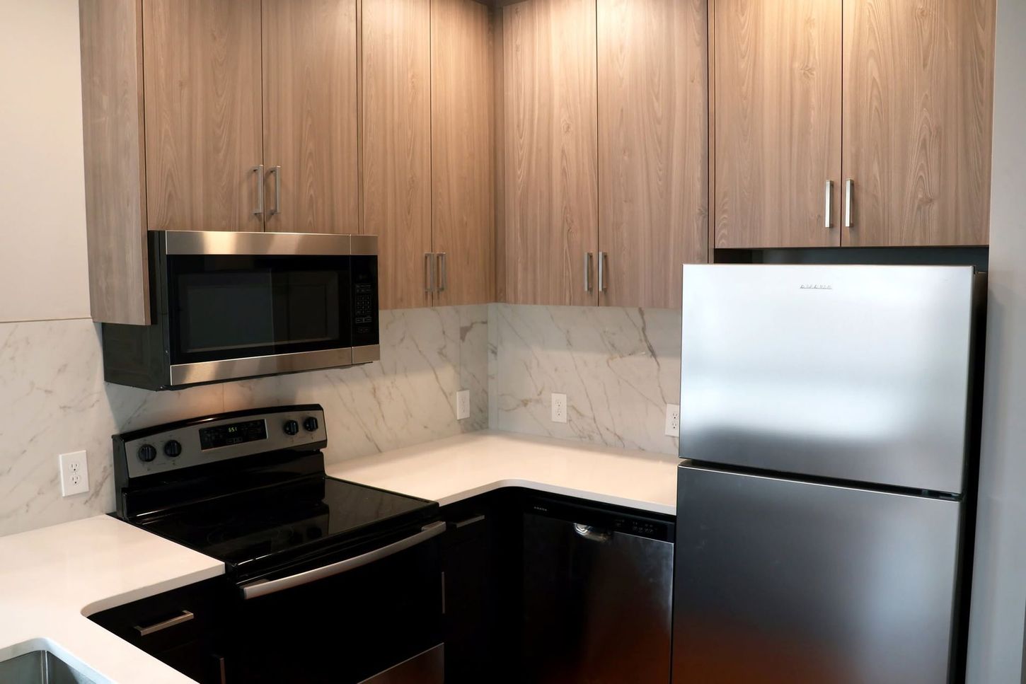 Modern kitchen with wood cabinets, black stove and microwave, white countertops, and stainless steel refrigerator