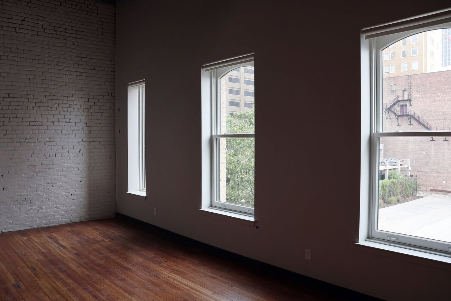 Empty room with dark walls, wood floor, and three tall windows letting in daylight