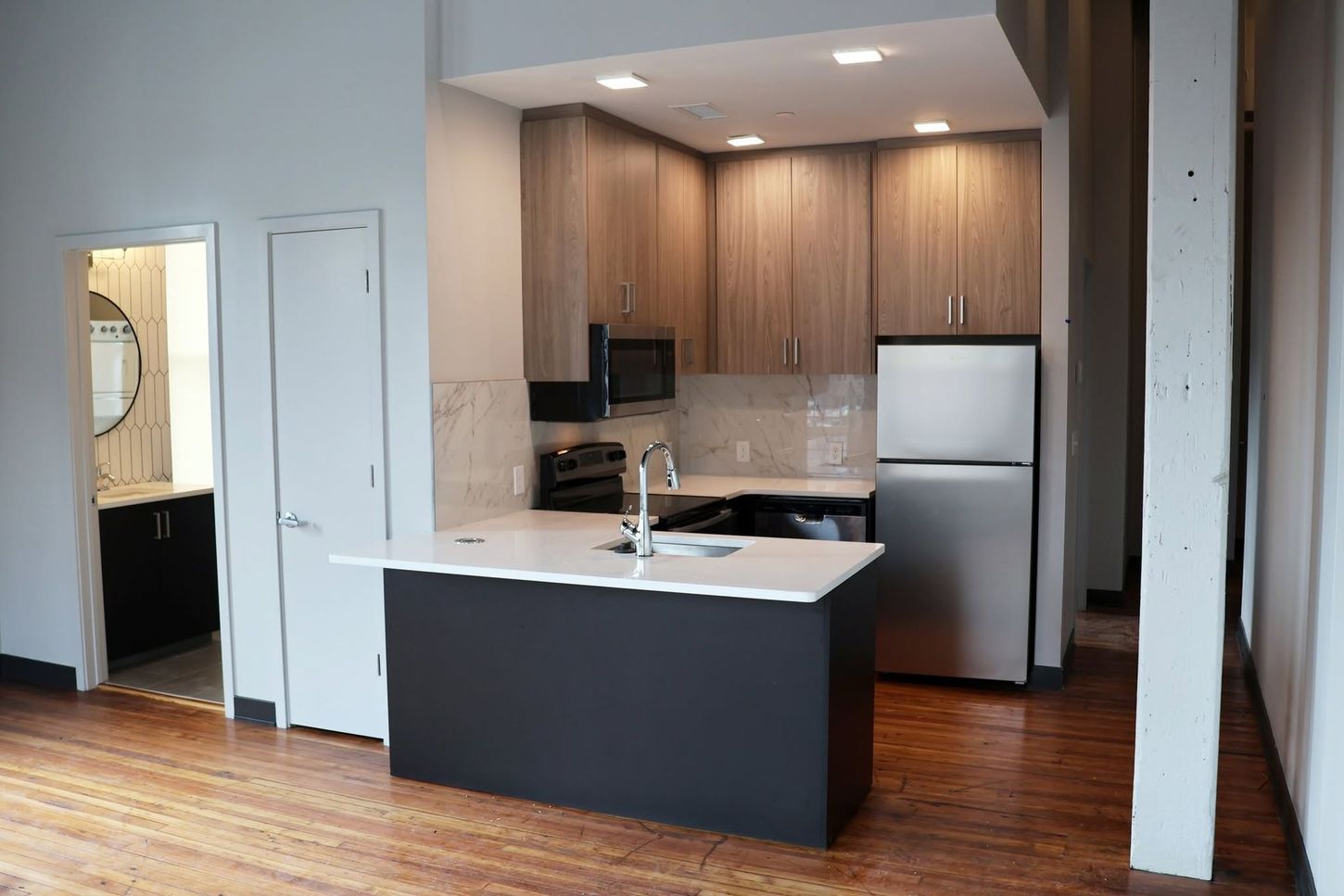 Modern kitchen with dark island, wood cabinets, stainless fridge, and hardwood floors