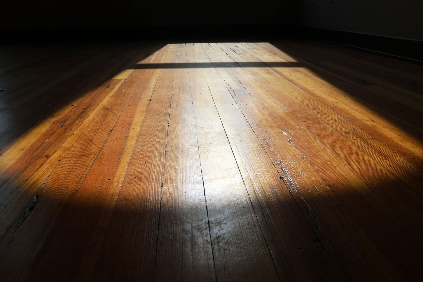 Sunlit wooden floorboards with a bright rectangular patch of light and dark surroundings
