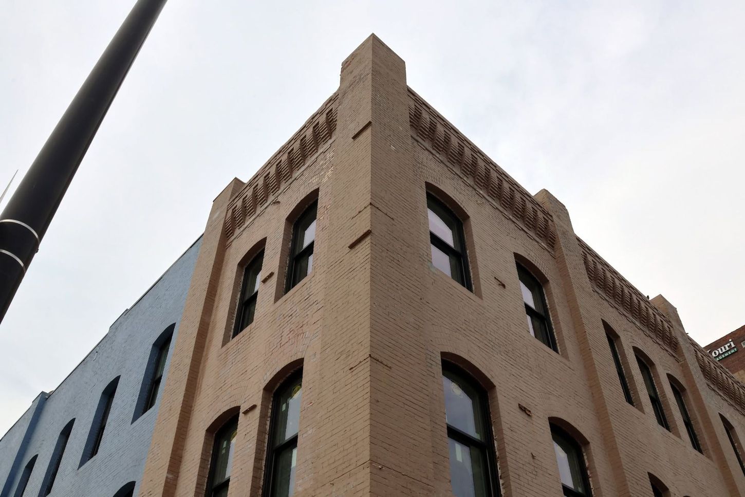 Corner of a tan brick building with arched windows against a cloudy sky