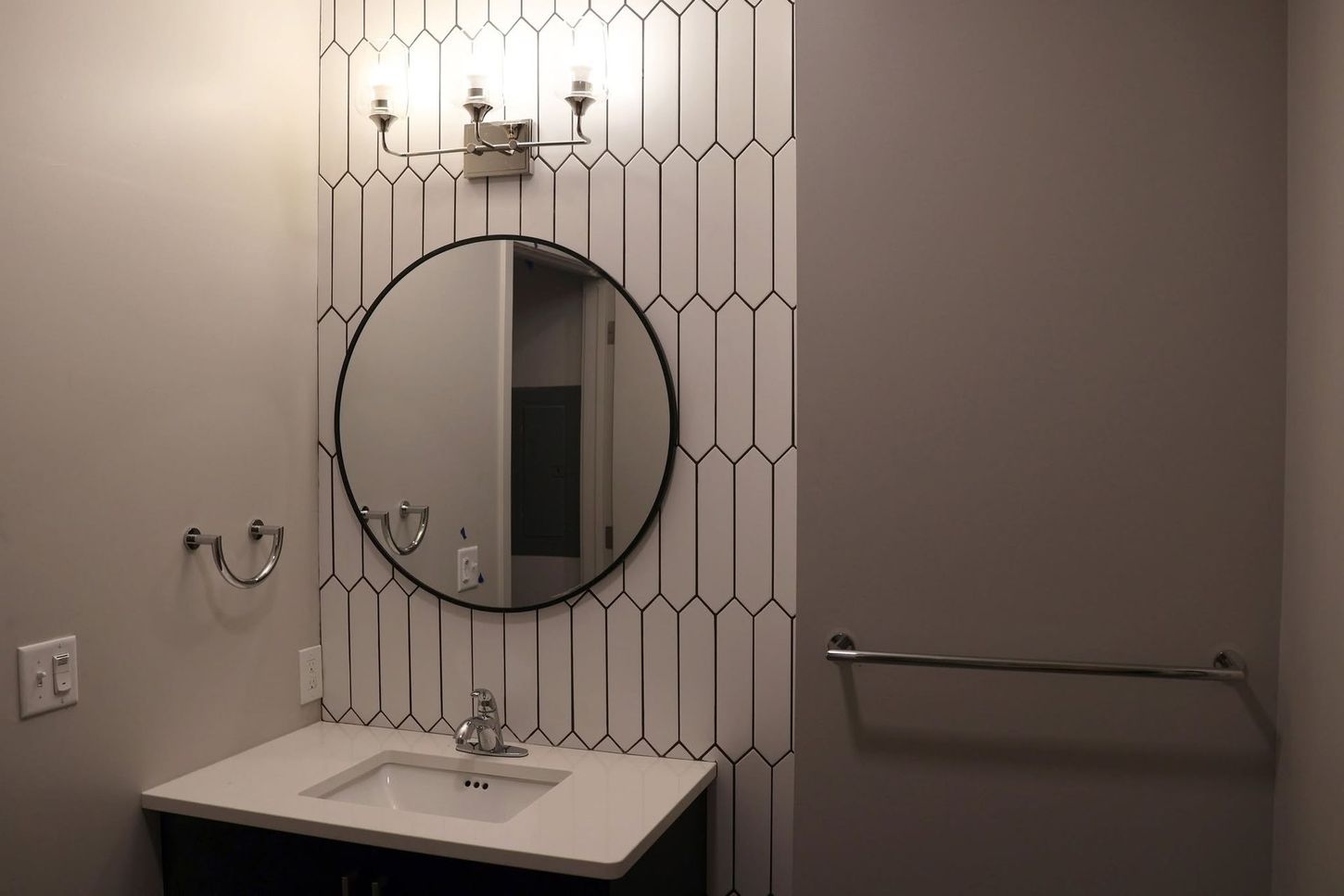Small bathroom vanity with round mirror, sconce light, and towel bar on gray wall