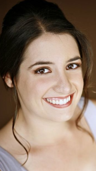Woman with dark hair smiling, wearing a light-colored top, with a soft background.