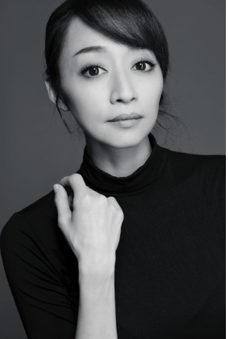 Woman in black turtleneck, holding her arm, with serious expression, monochrome photo.
