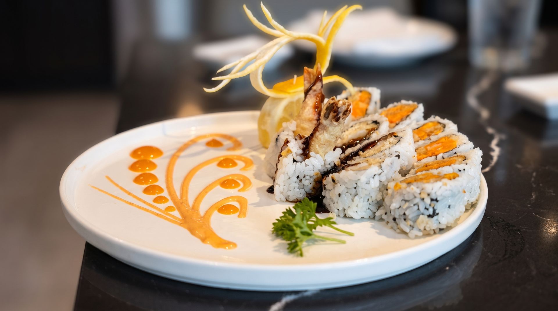 Sushi rolls on a white plate with orange sauce drizzle and garnish on a dark table