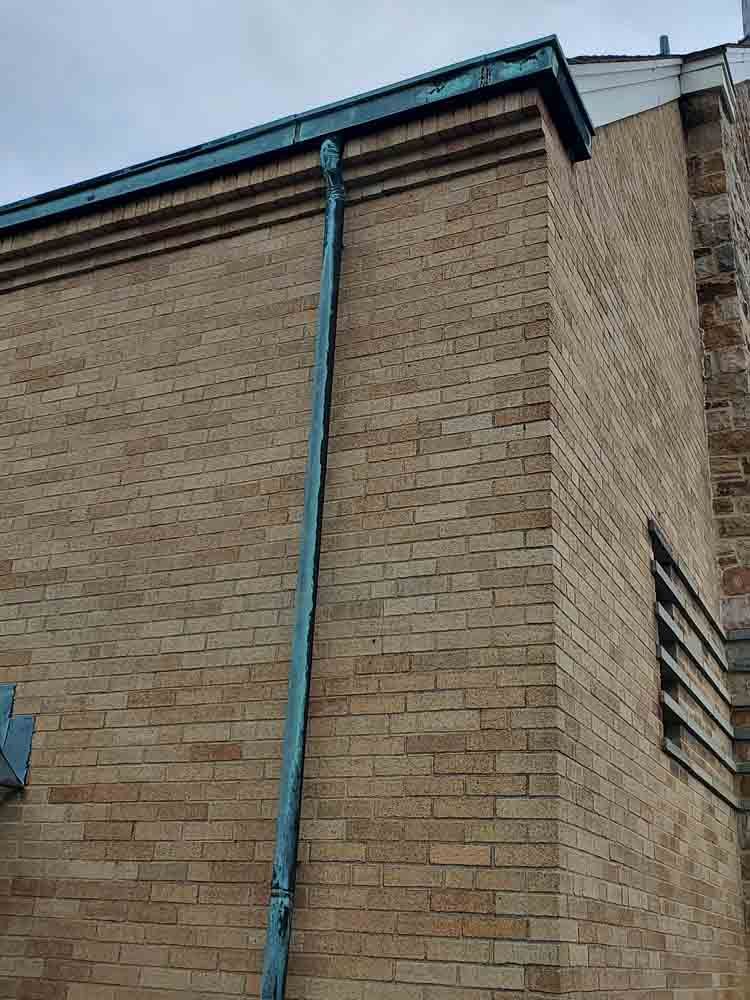 Brick building exterior with a blue downspout under a roof edge