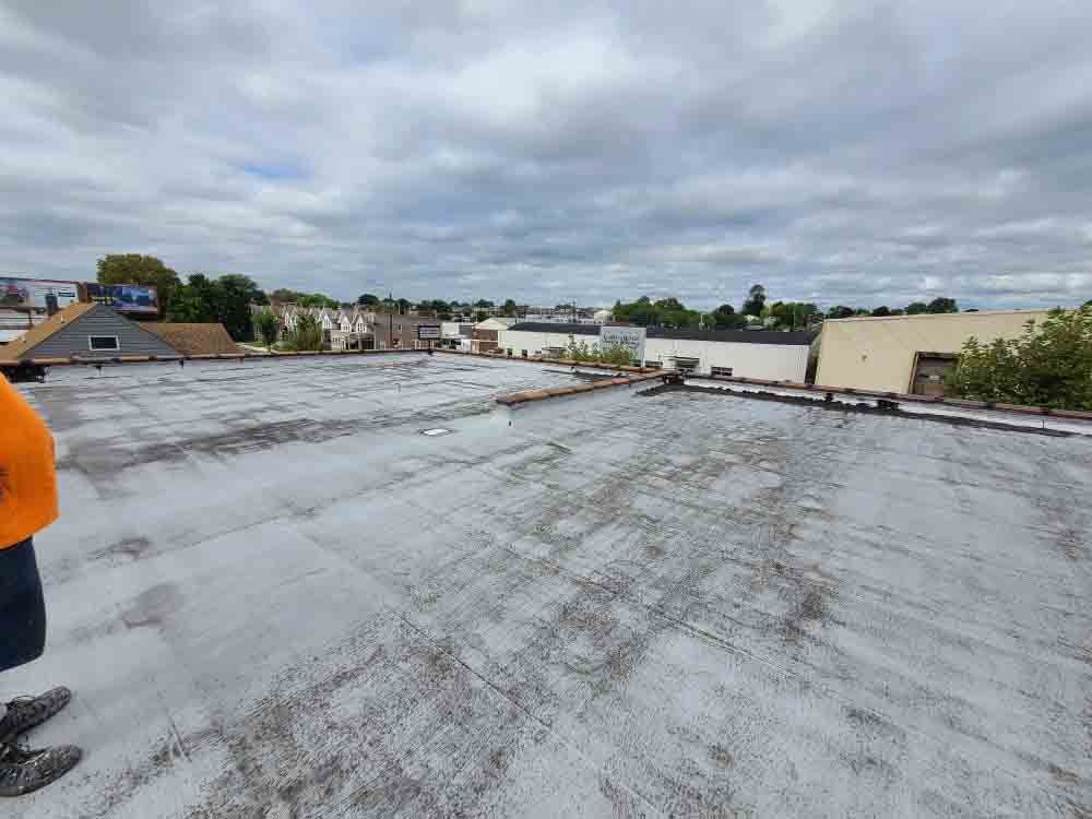 Rooftop with weathered gray surface under cloudy sky, buildings in the distance, and a person partially visible at left.