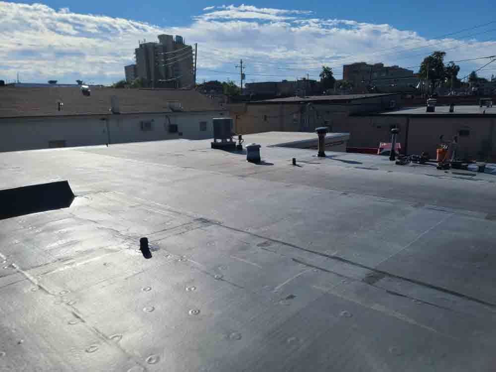 Rooftop with white surface, vents, and low buildings under a bright blue sky