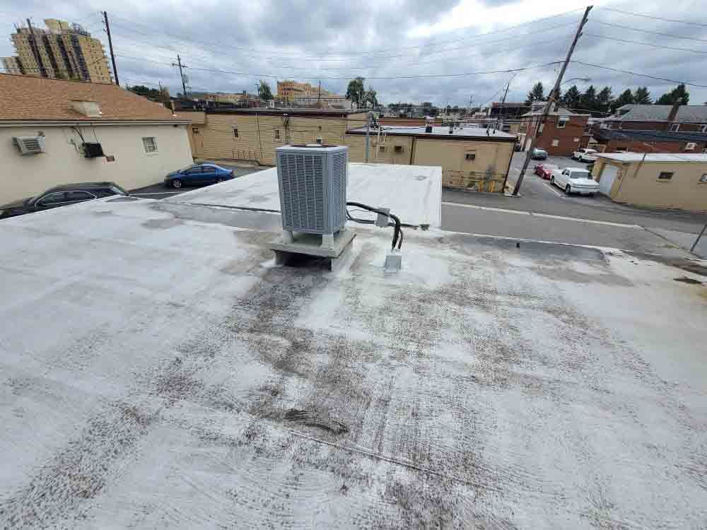 Rooftop with a large HVAC unit on a flat white roof, overlooking nearby buildings and a cloudy sky