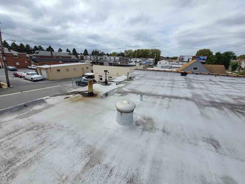 Flat rooftop with vents and HVAC units overlooking a small town under cloudy skies.